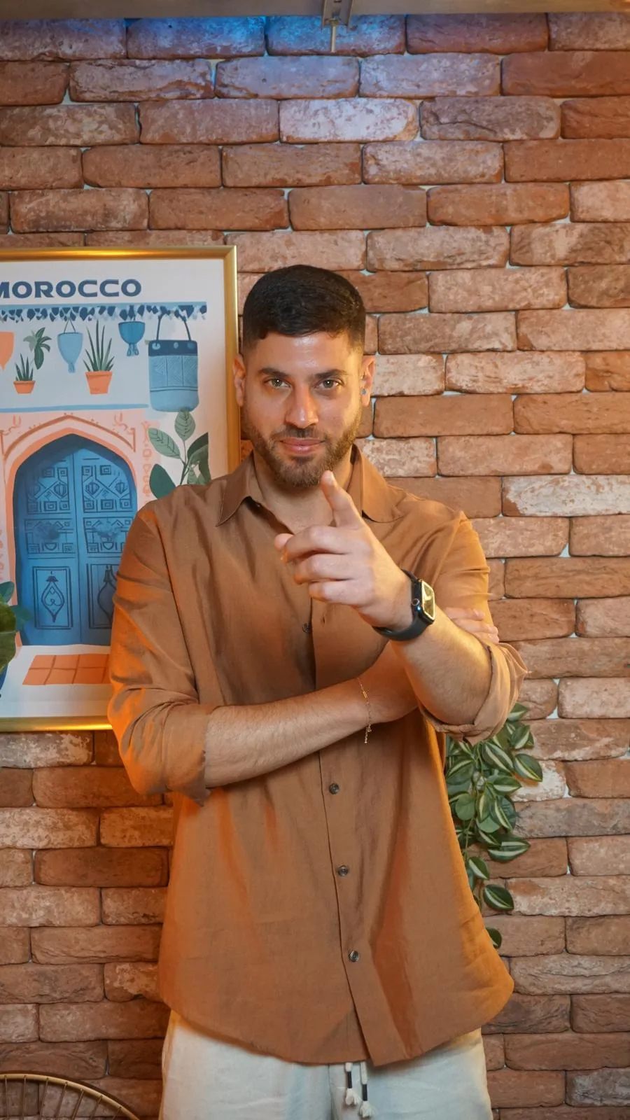 אלירן עזר בחולצה חומה על רקע קיר לבנים